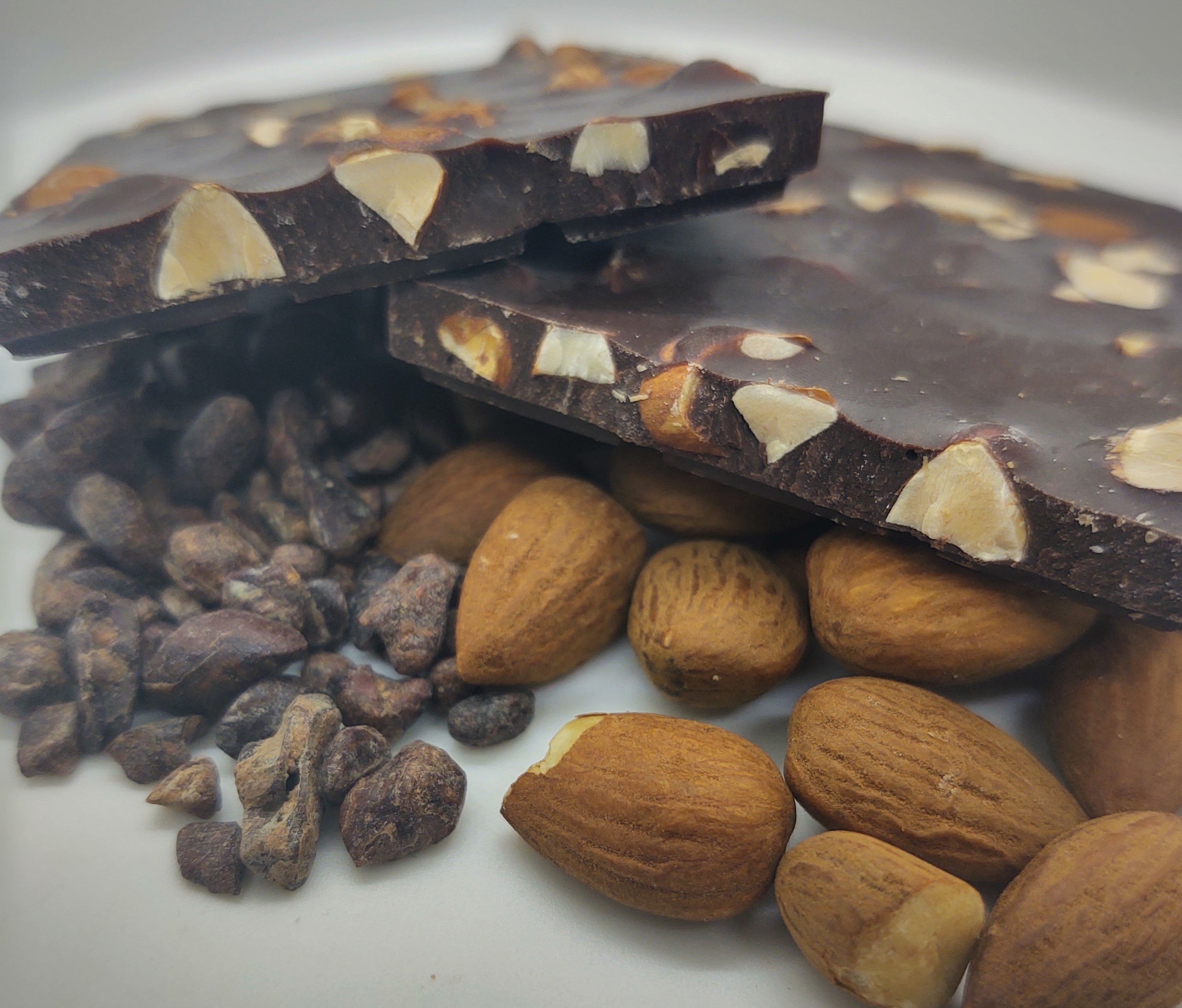 Pictured: solid dark chocolate bar with almonds. The bar is mounted by cocoa nibs and whole, roasted almonds