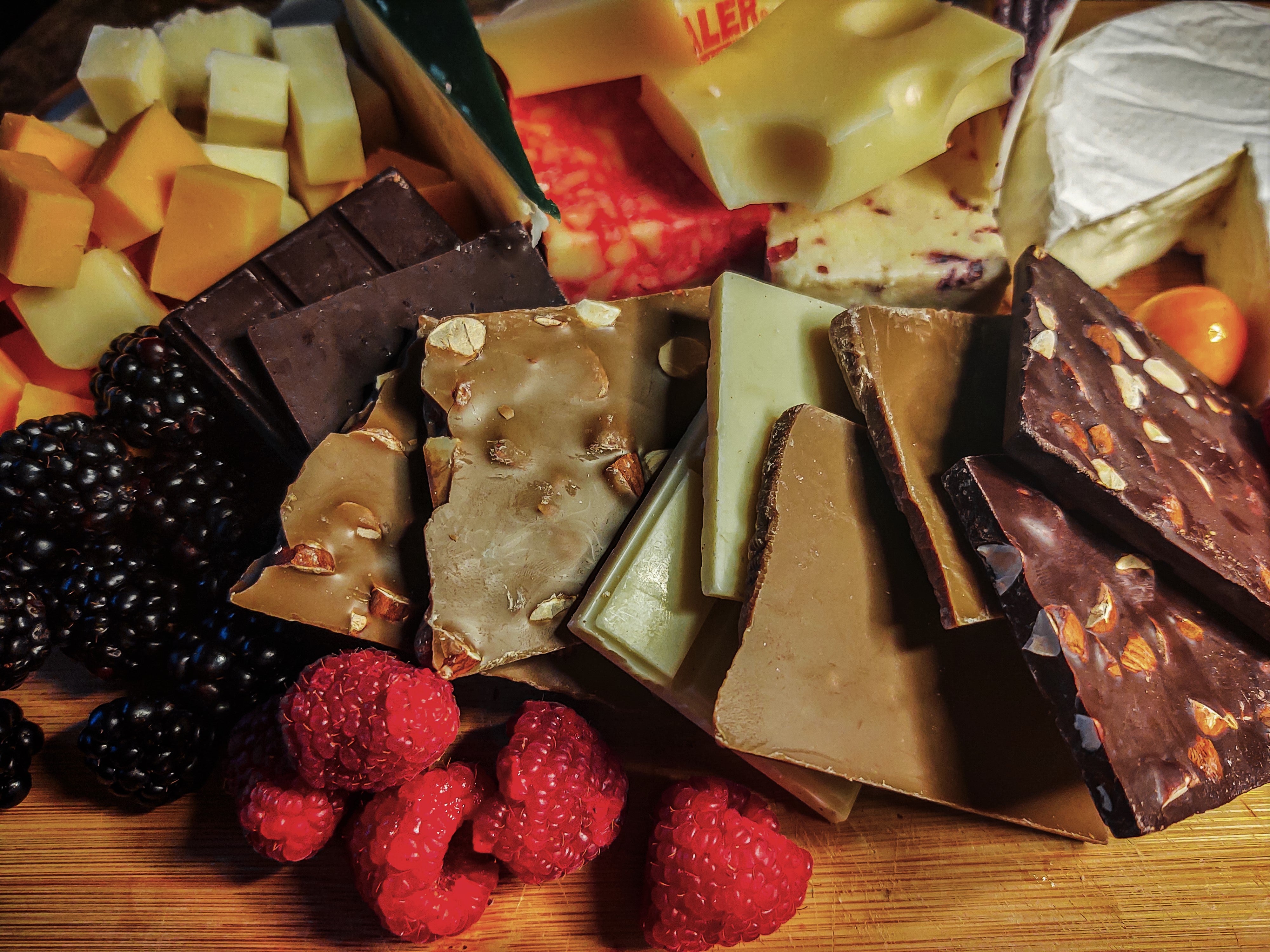Pictured: a charcuterie board filled with various fruits and cheeses. In the center of the board are all five flavor offerings from the Simplicity Chocolate brand.